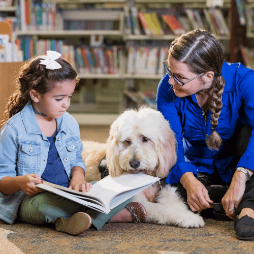Therapy dog sitting with a child and adult reading